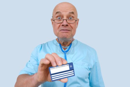 Photo for Frightened elderly physician with an expressive facial expressions plaintively shows electronic public health insurance cheaper, Insurance Card EU, concept healthcare coverage abroad, healthcare cost - Royalty Free Image