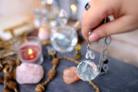 Frauenhand mit Kristallglaskugel, Pendel schwingt über den Tisch der Astrologin, Harmonie mit Meditation, Selbstfindung, Spirituelle Energie und Balance, Wahrsagerei und Wahrsagerei, Magie und Erwachen