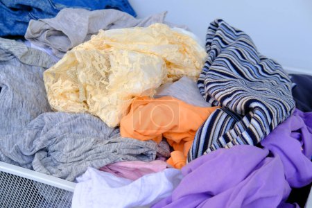 Photo for Colorful clothes randomly lying around in mesh basket close-up, mess, chaos in dressing room, concept of minimalism, simplicity, reducing clutter in one's living space, Sustainable living - Royalty Free Image