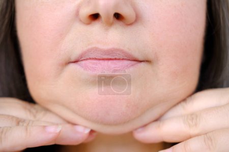 close-up of charismatic mature woman 50 years old looks carefully examines double chin, skin folds, age-related skin changes, aesthetic injection cosmetology, care anti-aging procedures