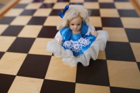 Foto de Juguete viejo, muñeca de porcelana Alice de fábrica alemana en miniatura interior con tablero de ajedrez, concepto de infancia estropeada, terapia de títeres - Imagen libre de derechos