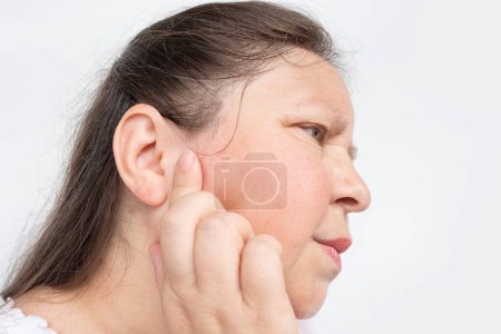 Photo for Mature woman 50-55 years old holds on to ear, close up female face with facial expression suffering, Ringing in ears, tinnitus, Inflammation of middle ear, acoustic trauma - Royalty Free Image