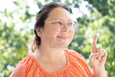 Photo for Pensive pretty woman 40-45 years old in glasses smiling, shows hand, pointing something with finger, Teaching and Instruction, Gesture and Communication, Cultural and Societal Influences - Royalty Free Image