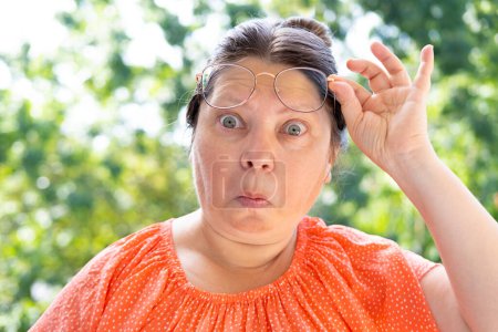 Photo for Displeased woman in glasses looks through lenses in surprise, Humorous Facial Expressions, middle-aged mature woman with bulging eyes, surprised, shocked by news, event - Royalty Free Image