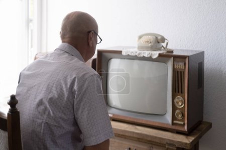 Foto de Anciano se enciende y mira la vieja televisión analógica retro con pantalla en blanco para el diseñador, fondo blanco, 1960-1970, maqueta elegante, plantilla para video, tecnología retro en la vida cotidiana - Imagen libre de derechos