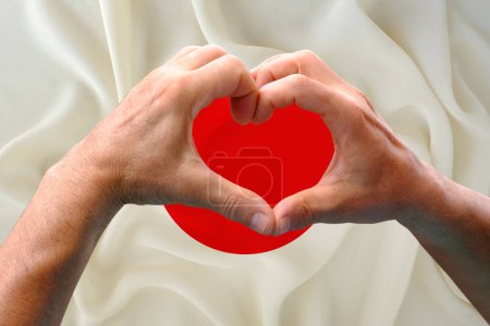 Téléchargez les photos : Gros plan des mains masculines en forme de cœur sur fond de drapeau national en soie du Japon, patriotes du concept de pays, fête de l'indépendance, voyage, coopération internationale - en image libre de droit