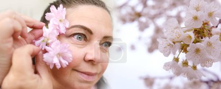 Photo for Close up female face in flowers, small wrinkles around eyes, human eyes looking to side, concept of beauty and cosmetic anti-aging procedures, vision examination, human health, plant pollen allergy - Royalty Free Image