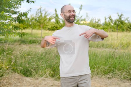 Photo for Satisfied young man 30-35 years old in light t-shirt, stylish glasses against natural background, Youth Culture and Stereotypes, younger generation, including clothing, accessories, outdoor activities - Royalty Free Image