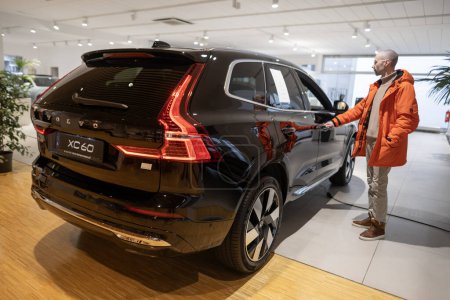 Photo for Young man examines, chooses new black Volvo XC60 Recharge Plug-in Hybrid SUV, Swedish car, High Tech Advanced technology in automotive industry show in Frankfurt, Germany - January 22, 2024 - Royalty Free Image