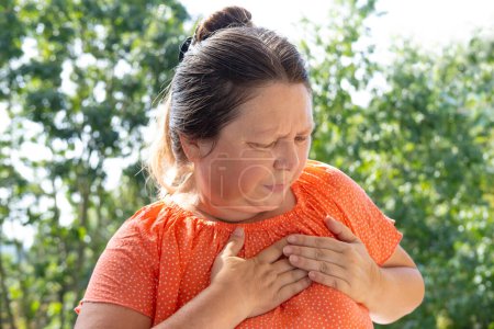 reife Frau im Alter von 50-55 Jahren hält sich am Herzen, plötzliche Brustschmerzen, weibliches Gesicht aus nächster Nähe mit Gesichtsausdruck leiden, ischämische Herzkrankheit, arterielle Hypertonie, Myokarditis oder Arrhythmie