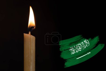 mourning candle burning front of flag Saudi Arabia, text Arabic testify there no other God but Allah, memory of heroes served country, grief over loss, national unity in challenging times
