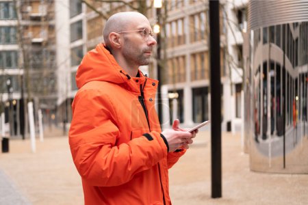 joven en chaqueta naranja brillante utiliza teléfono inteligente contra el telón de fondo de las calles de invierno de Berlín, Tecnología y vida urbana, Comunicación moderna, Nomadismo digital, uso de dispositivos