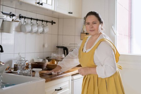 mature woman housewife, housekeeper in yellow linen apron, smiling efficiently cleans kitchen, maintaining clean and organized home, clean organized home source pride and satisfaction for homeowners