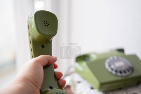Foto de Auricular de mano femenina de teléfono verde, teléfono giratorio con esfera de disco, antigüedades bien mantenidas, tecnología obsoleta, estética retro 80 - Imagen libre de derechos