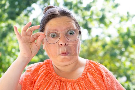 surprised, shocked by news, event woman 50 years old with long hair, close up female face, funny woman in glasses looks through lenses in surprise, Comedic Performance and Expression