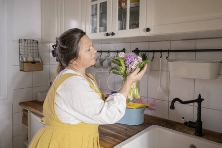 happy mature woman with beautiful bouquet of hyacinths in kitchen, spring home cleaning, highlighting satisfaction in freshness and beauty spring