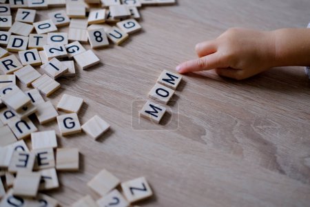child's small hands carefully arrange wooden letters to spell Mom, heartwarming expression of love and appreciation, Early Literacy Development