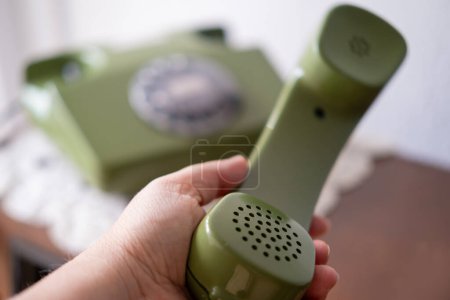 weibliche Hand hält Hörer von grünem Telefon, Rotationstelefon mit Scheibenwahl, Gepflegte Antiquitäten, veraltete Technologie, Retro-Ästhetik der 80er Jahre