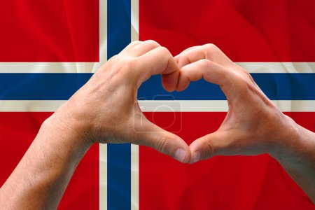 Téléchargez les photos : Gros plan des mains masculines en forme de cœur sur fond de soie drapeau national de l'État européen de Norvège, patriotes du concept de pays, fête de l'indépendance, voyage, coopération internationale - en image libre de droit