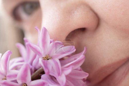 close-up Female face light with delight schmeckt süß duftende Hyazinthe, fängt die Freude am Frühling und der Schönheit der Natur ein und sensibilisiert gleichzeitig für saisonale Allergien, Sinneserlebnisse