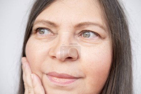 mature woman gently touches face, accepting visible signs aging such wrinkles, sagging skin and changing facial shape with grace and self-love, self-discovery, self-acceptance ages