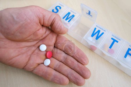 Nahaufnahme von Medikamentenkapseln, Pillen, Vitaminen in der männlichen Handfläche, Plastik-Pillbox-Organizer für die Woche, Konzept zur Kontrolle der regelmäßigen Medikamenteneinnahme, Medikamentendosierung, Organisation der Medikamenteneinnahme