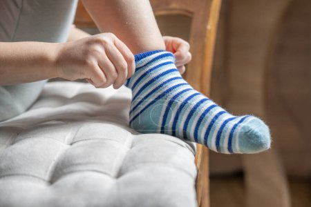 close-up child, girl 4 years old learning to dress independently, putting on blue striped sock, Young kid achieving self-dressing milestones, Fine motor development, Self-care skills