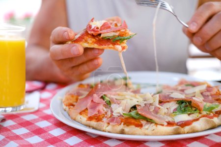 round italian pizza cut into slices on table, male hands take pieces of pizza with salami, cheese, arugula, hands with food close-up, concept family pleasure, culinary tradition, food tourism