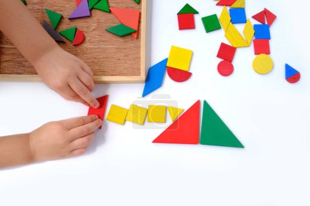 smart little child, girl 3 years old playing with educational toy, wooden geometric figures, wooden puzzles, children's hands create pictures from colored wooden geometric shapes