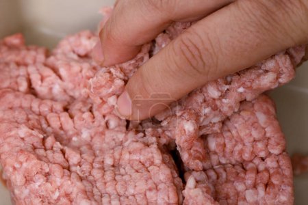 closeup female hand kneads minced meat, raw fresh minced meat with fat from pork, beef, lamb, concept of cooking at home in kitchen