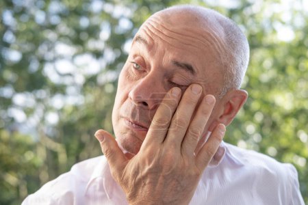 man 60-65 years old, senior crying, suffering, fatigue syndrome eye Asthenopia, eye pain symptoms, including strain, allergies, severe eye conditions, corneal ulcers, glaucoma or acute angle-closure