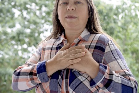 Frau 45-50 Jahre alt im karierten Hemd hält Herz, plötzliche Brustschmerzen, aus der Nähe weibliches Gesicht mit Gesichtsausdruck leiden, ischämische Herzkrankheit, arterielle Hypertonie, Myokarditis oder Arrhythmie