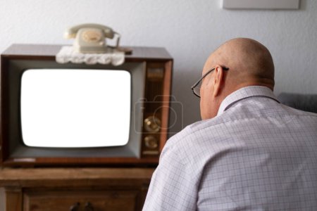 Foto de Anciano se enciende y mira la vieja televisión analógica retro con pantalla en blanco para el diseñador, fondo blanco, 1960-1970, maqueta elegante, plantilla para video, tecnología retro en la vida cotidiana - Imagen libre de derechos