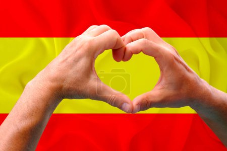 Nahaufnahme männlicher Hände in Herzform vor dem Hintergrund der seidenen Nationalflagge des europäischen Staates Spanien, Patrioten des Länderkonzepts, Unabhängigkeitstag, Reisen, internationale Zusammenarbeit