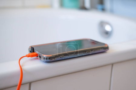 phone charging on edge of bathtub, concept Dangers Electronics in Wet Areas, Preventing Water-Related Accidents, Safe Charging Practices