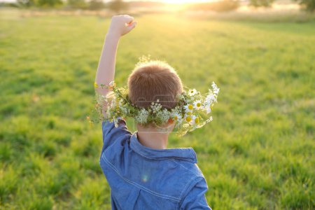 happy boy in wreath, floral crown on green sunlit meadow rear view, seen from behind, beauty nature and arrival summer, Midsummer celebration, tranquility nature, conveying sense awe, peace