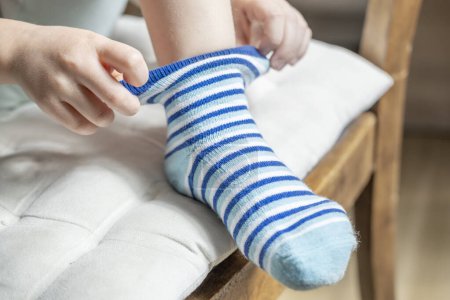close-up of female 4-year-old child, Preschooler learning to dress independently, putting on striped sock, Young kid achieving self-dressing milestones, Fine motor development, Self-care skills