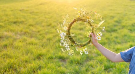 floral crown, wreath in male hand on green sunlit meadow, seen from behind, beauty nature and arrival summer, carefree summer days, Midsummer celebration, wiccan Litha sabbat, pagan holiday