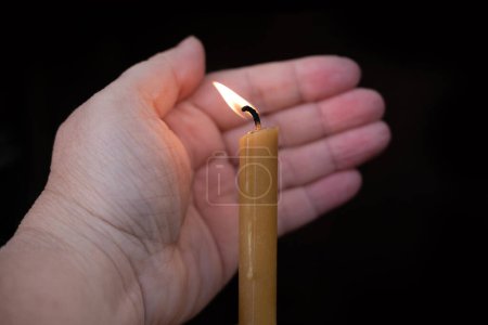 Close-up candle in dark, female hands shield burning flame from wind, religious ceremonies and mourning rituals, solemnity and remembrance, spiritual meditation
