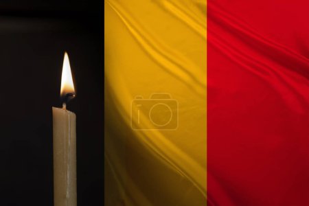 mourning candle burning front of flag Belgium, memory of heroes served country, grief over loss, national unity in challenging times, state's history