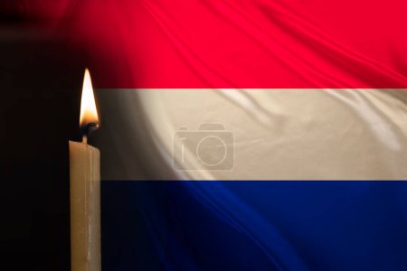 mourning candle burning front of flag Netherlands, memory of heroes served country, grief over loss, national unity in challenging times, state's history
