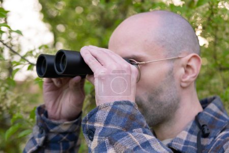 man, hidden in lush greenery spies clad peers through binoculars, private investigator conducts surveillance, thrill-seeker tracks down target