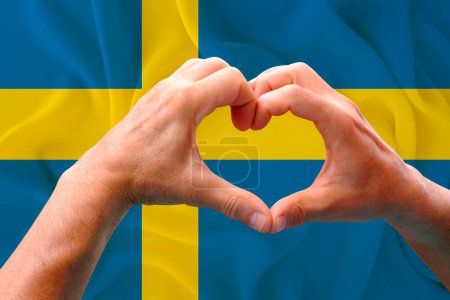 Téléchargez les photos : Gros plan des mains masculines en forme de cœur sur fond de soie drapeau national de l'Etat européen de Suède, patriotes du concept de pays, fête de l'indépendance, voyage, coopération internationale - en image libre de droit