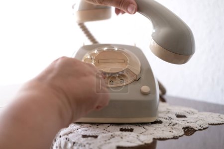 mature female hand removing Handset, rotating Dialer on Old white Rotary Telephone with Disc Dial with finger, putting retro phone reciver down, hanging up, calls helpline, psychological support