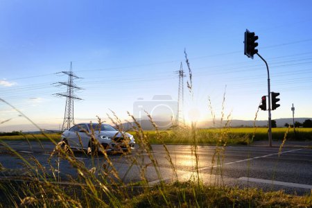 beautiful dramatic landscape, car road visible behind grass, power towers, field in evening in rays sunset, concept beauty of nature, modern energy, technology, seasonal change