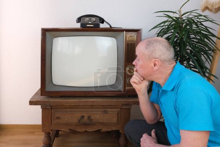 homme âgé en polo bleu s'assoit sur le sol devant la vieille télévision analogique rétro, télévision, maquette d'écran blanc pour designer, Regarder la télévision, Style de vie des personnes âgées