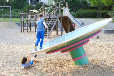 zwei Jungen, Kinder 9-10 Jahre spielen auf dem Spielplatz, versuchen das Gleichgewicht auf der Unruh zu halten, lustiges Stück Gleichgewichtsgerät für Spielplätze, glückliche, sichere Kindheit