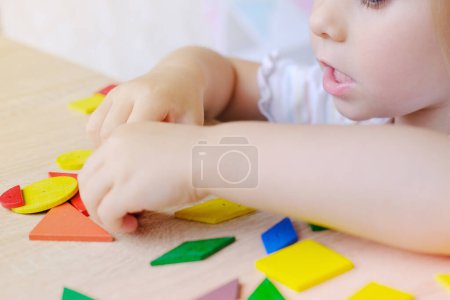 niedliches Kind, Mädchen 3 Jahre alt spielt mit farbigen geometrischen Holzfiguren, zählt Details, Konzept der Entwicklung von Kreativität, Feinmotorik, Geduld Ausdauer, Kinderunterhaltung