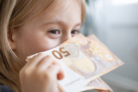 weibliches Kind, fröhliches Mädchen hält 50-Euro-Scheine in Nahaufnahme, Fantasie beflügelt Powergeld, Finanzbewusstsein, glücklicher Junge