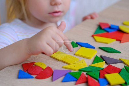 Litle cute child, girl plays with colored wooden geometric figures, cubes, builds houses and animals, counts details, concept of development of creativity, fine motor skills, patience perseverance